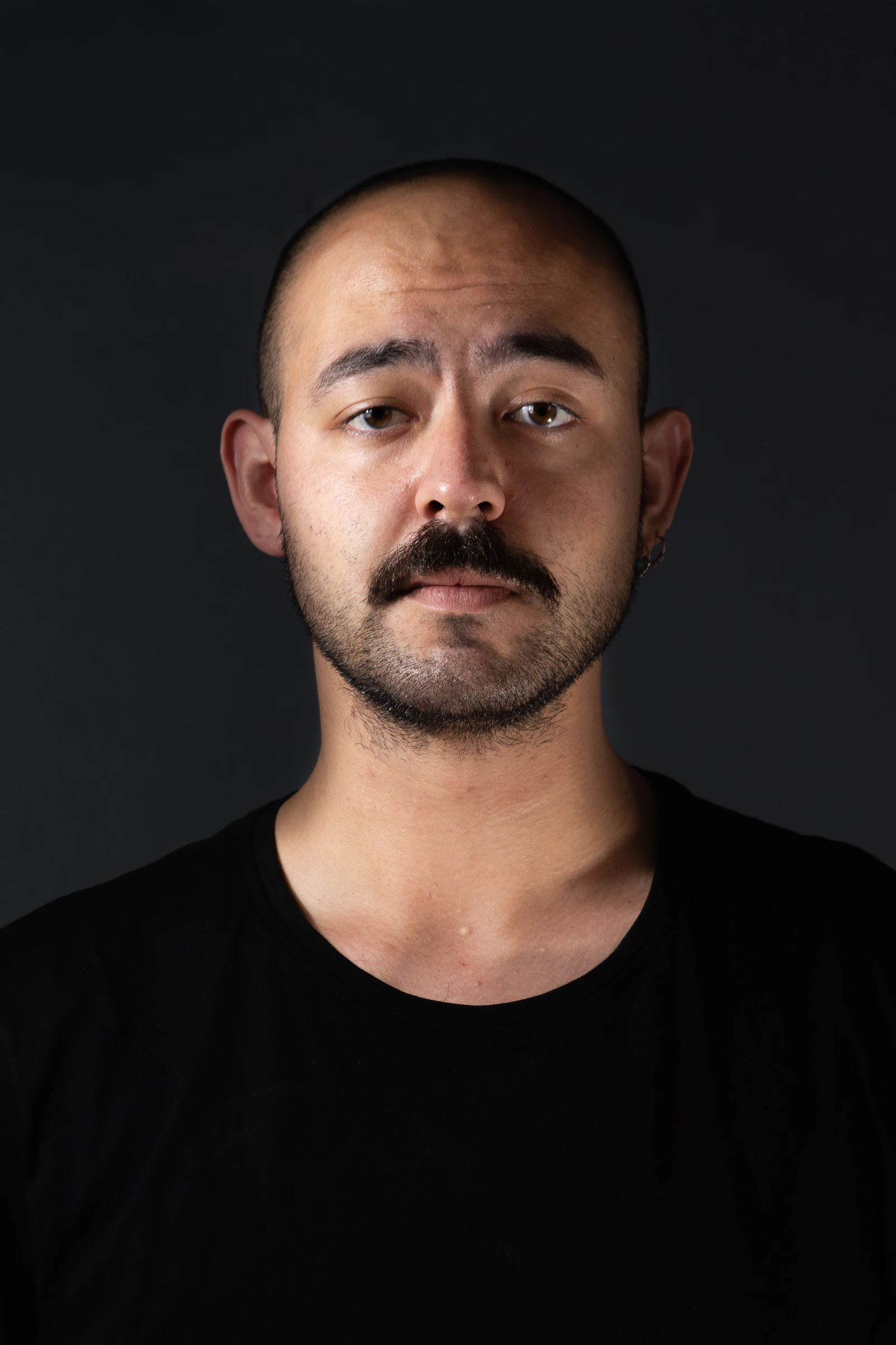 Man in his thirties with a closely cropped buzz cut against a black background