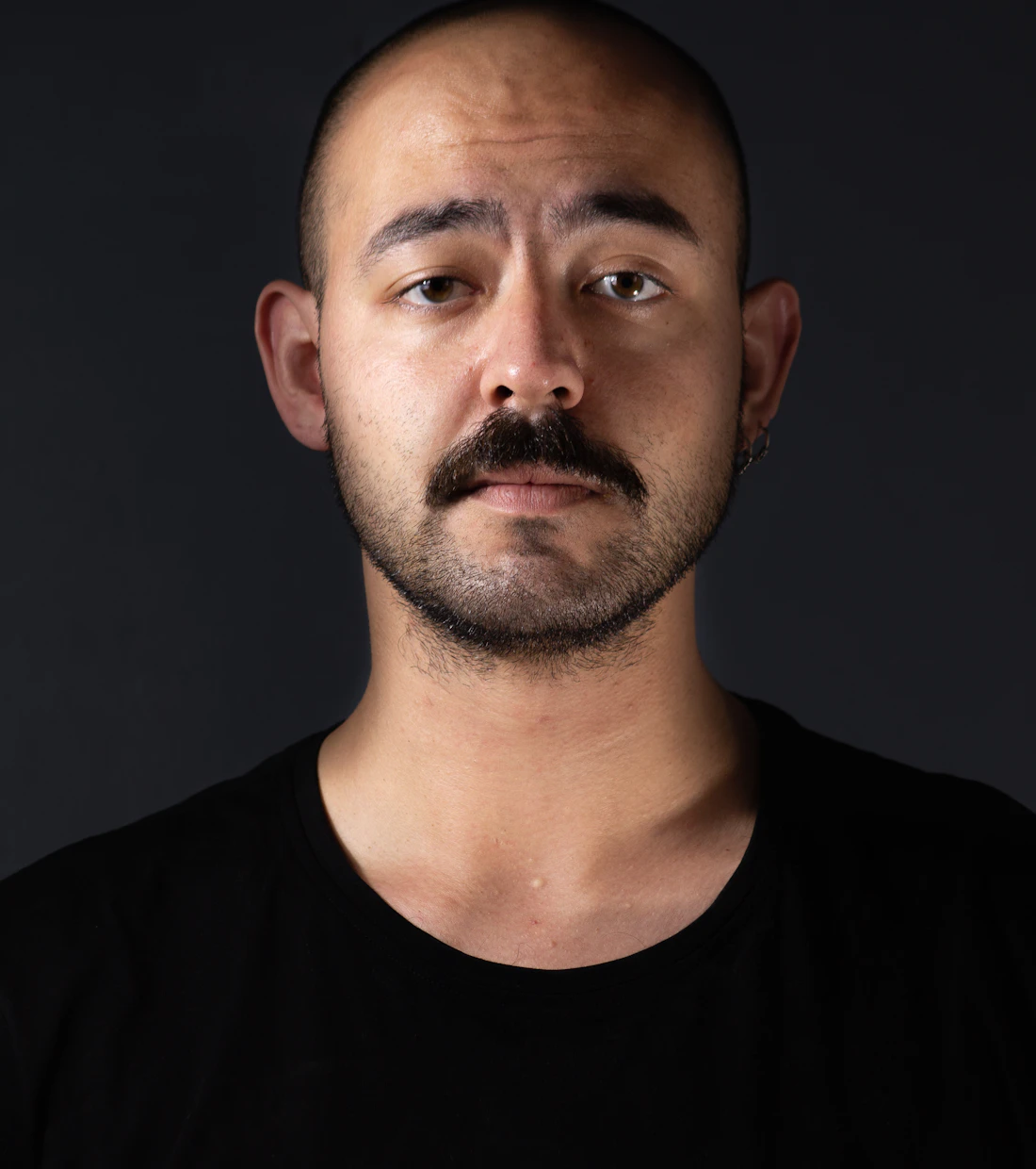 Man with a closely cropped buzz cut against a black background