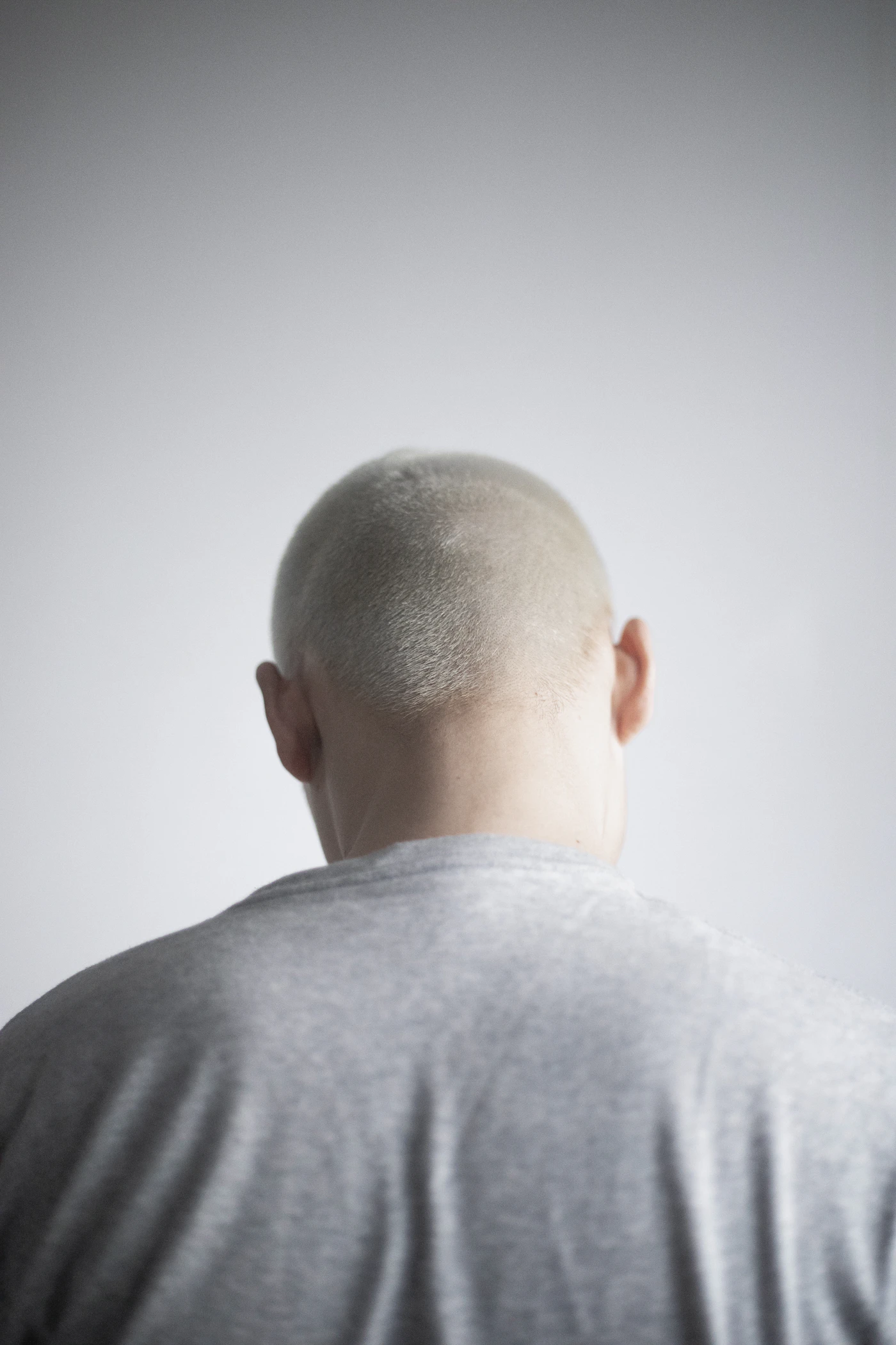 Man with a shaved head facing a white wall