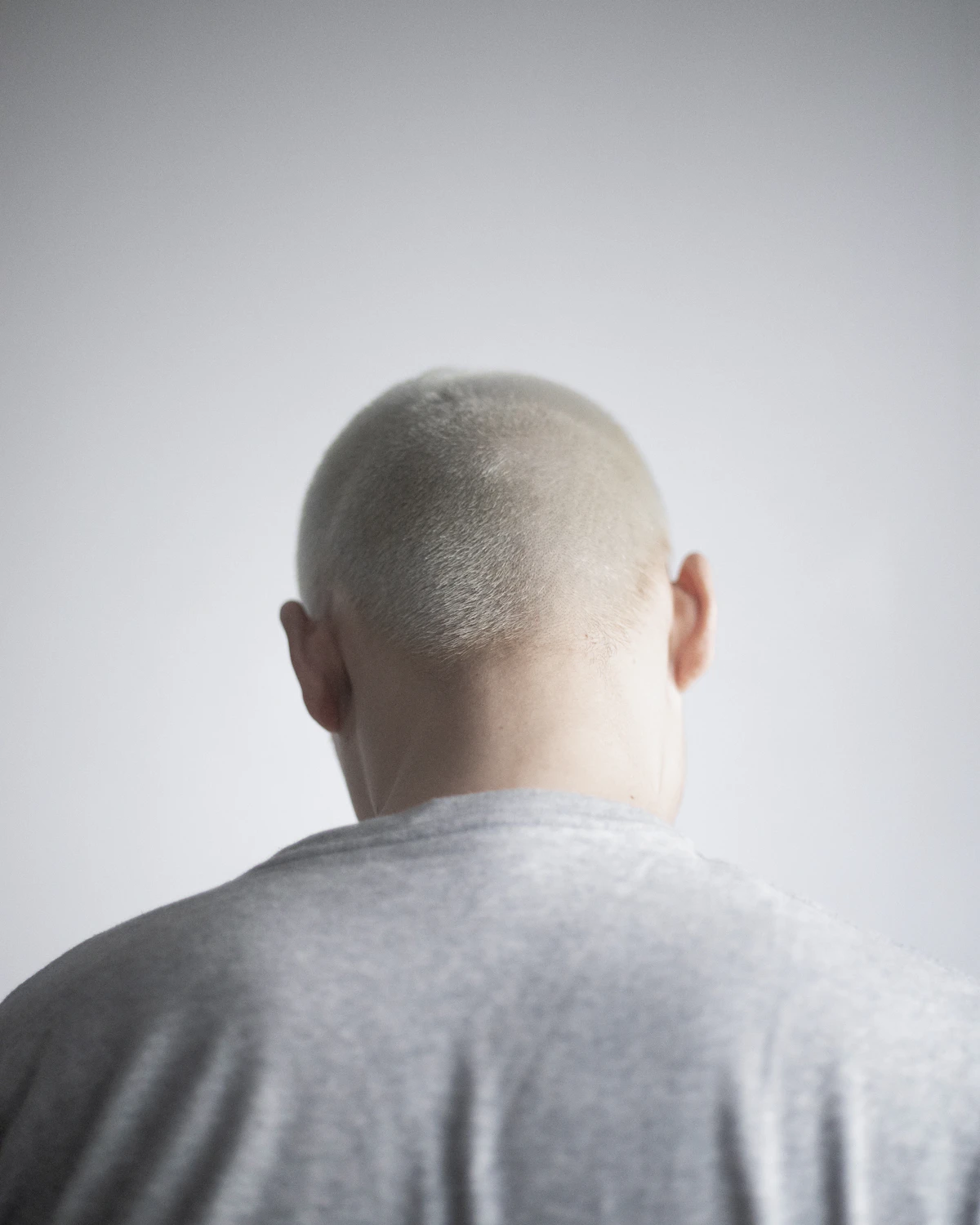 Man with a shaved head facing a white wall